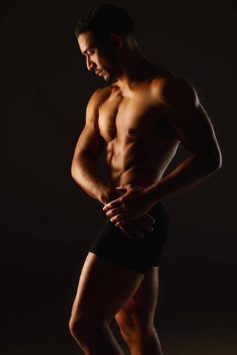 纪律最强的肌肉工作室拍摄适合年轻的男人。摆姿势黑色的背景