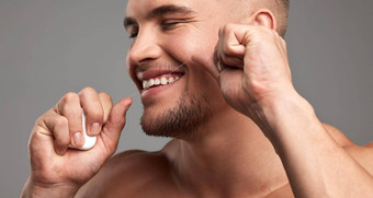 牙线老板工作室拍摄英俊的年轻的男人。用牙线清洁牙齿牙齿灰色背景