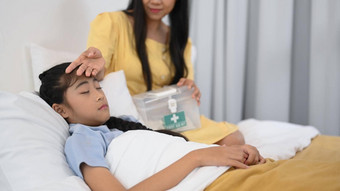 生病的亚洲女孩高发热睡觉床上妈妈。检查温度额头爱护理家庭为人父母概念