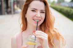 年轻的美丽的红发女人牙套饮料冷却柠檬水在户外夏天肖像微笑女孩雀斑