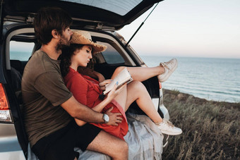 男人。女人坐着内部打开树干运动型多功能车车年轻的夫妇享受路旅行海日落