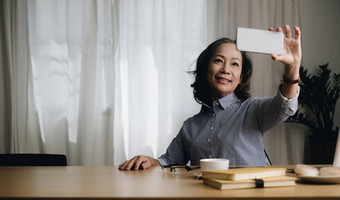 亚洲高级上了年纪的女人微笑视频调用生活房间首页强大的上了年纪的老祖母感觉快乐移动细胞电话沟通家庭享受退休生活房子