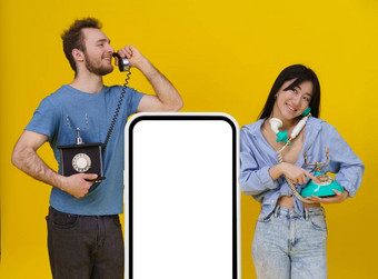 英俊的的家伙亚洲女孩会说话的古董手机靠巨大的智能手机数字平板电脑空白屏幕快乐微笑孤立的黄色的背景模拟产品放置