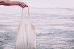 白色空白棉花生态手提包设计模型持有空白帆布手提包袋设计模型手工制作的购物手提包袋女孩海滩背景夏天的想法