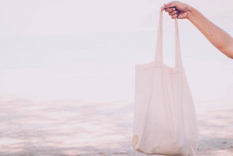 白色空白棉花生态手提包设计模型持有空白帆布手提包袋设计模型手工制作的购物手提包袋女孩海滩背景夏天的想法
