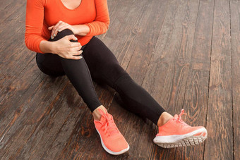 女人持有痛苦的膝盖坐着地板上首页健身房痛苦肌肉应变扭伤韧带