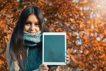 女孩显示屏幕平板电脑查看器站背景明亮的秋天树叶公园
