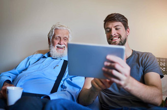 欢迎爷爷年龄技术拍摄年轻的男人。显示上了年纪的祖父平板电脑坐着沙发上首页