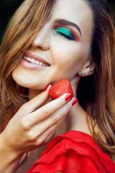 年轻的美丽的快乐有趣的女孩红色的衣服化妆持有草莓夏季公园