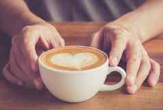 手男人。咖啡师持有杯热咖啡拿铁心形状的泡沫艺术