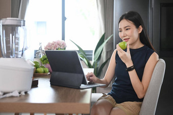 美丽的亚洲女人浏览互联网移动PC吃<strong>苹果首页</strong>厨房