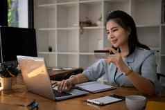 年轻的亚洲女人办公室工人持有信贷卡购物在线电脑移动PC