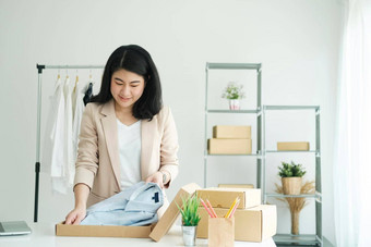 亚洲女衣服商店老板折叠t恤包装纸板包裹盒子