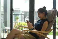 年轻的亚洲女人坐着舒适的扶手椅首页移动电话