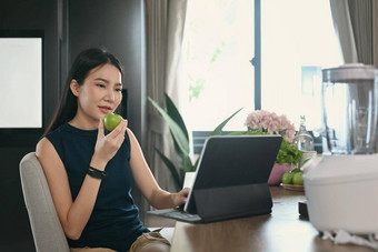 健康的年轻的女人吃苹果电脑平板电脑厨房