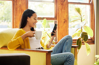 拉美裔女人智能手机喝咖啡坐着前面窗口明亮的生活房间一边配置文件年轻的女手机放松椅子首页