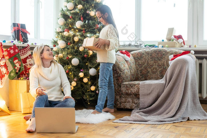 室内拍摄美丽的快乐年轻的女人购物在线移动PC舒适的圣诞节室内妈妈。地板上圣诞节树沙发女儿拥抱购物礼物