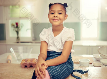 肖像可爱的年轻的混合比赛女孩坐着厨房计数器微笑穿围裙深思熟虑的无辜的拉美裔女孩微笑坐着烘焙厨房首页烘焙爱好白日梦日常