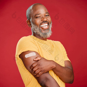 成熟的非洲美国男人。胡子微笑快乐穿邦迪牌<strong>创可贴</strong>持有手臂站红色的工作室背景疫苗接种健康医疗保健