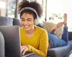 年轻的快乐的混合比赛女人穿耳机听音乐移动PC首页快乐拉美裔女卷曲的非洲式发型打字电脑放松沙发上首页