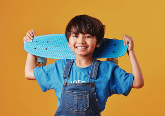 可爱的亚洲男孩快乐持有滑板橙色背景可爱的男孩穿休闲衣服微笑携带滑板可爱的孩子有趣的