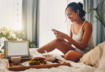 美丽的年轻的拉美裔女人检查社会媒体手机享受床上早餐酒店