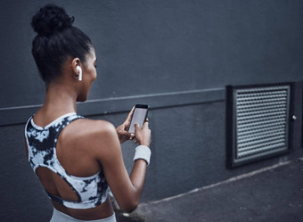 特写镜头年轻的混合比赛女人听音乐无线耳机手机空白屏幕打破锻炼在户外黑暗背景女运动员发短信健身应用程序在线浏览社会媒体