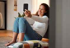年轻的女人采取自拍手机女孩坐着地板上采取照片微笑年轻的女人采取自拍智能手机女人移动电话首页