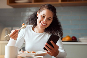 女人吃寿司手机年轻的女人发送文本智能手机吃海鲜快乐女人享受餐首页年轻的女孩吃可口的鱼