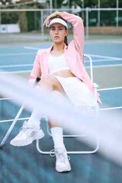 时尚的年轻的网球球员穿粉红色的夹克坐着椅子网球法院年轻的拉美裔女运动员坐着网球球拍匹配