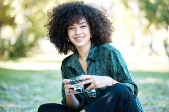 微笑年轻的摄影师享受一天公园坐着草采取照片数字相机快乐拉美裔女人卷曲的非洲式发型持有相机设备花园