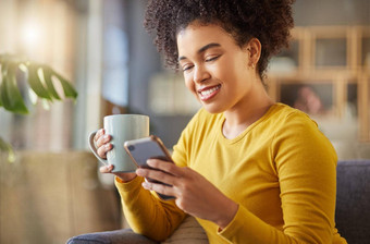 快乐混合比赛女人喝杯咖啡打字消息电话首页内容拉美裔女卷曲的非洲式发型社会媒体手机放松沙发上首页