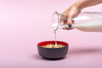 烹饪牛奶什锦早餐女人倒牛奶壶飞碟牛奶什锦早餐片粉红色的背景的地方插入文本大横幅打印广告