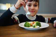 焦点蒸蔬菜健康的素食主义者食物模糊可爱的男孩持有叉微笑相机午餐自助餐厅