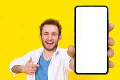 检查应用程序年轻的男人。指出智能手机显示白色空屏幕游戏打赌彩票赢得孤立的黄色的背景产品放置移动应用程序广告