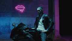 男人。bandama坐在体育摩托车太阳镜砖墙霓虹灯标志烟
