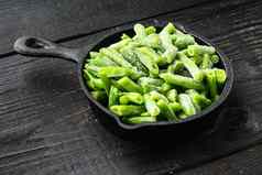 冻有机绿色豆子健康的食物概念煎投铁锅黑色的木表格背景