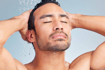 关闭肌肉发达的亚洲男人。洗澡洗头发蓝色的工作室背景适合强大的混合比赛男人。站倒水拉美裔运动员享受热淋浴眼睛关闭