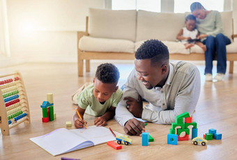 年轻的快乐非洲美国父亲帮助儿子家庭作业坐着地板上首页男孩集中学习任务小男孩画书
