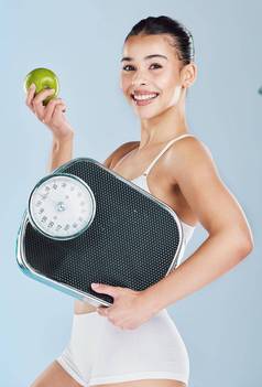 肖像快乐年轻的女人持有苹果规模蓝色的Copyspace背景自信运动适合女显示好处平衡饮食重量损失健康的生活方式