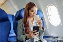 肖像成功的亚洲业务女人女企业家正式的西装飞机坐在业务类座位智能手机喝咖啡飞行放松概念