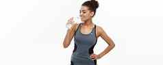 健康的健身概念美丽的非洲美国女孩体育运动衣服喝水塑料瓶锻炼孤立的白色工作室背景