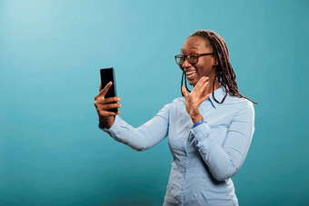 快乐微笑非洲美国女人智能<strong>手机</strong>挥舞着视频会议调用蓝色的背景