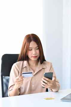 年轻的亚洲女人手持有信贷卡聪明的电话在线购物