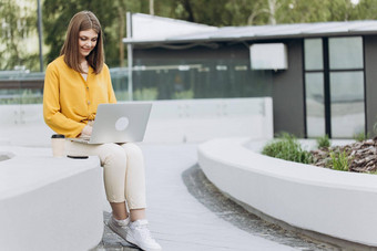忙工人自由职业者工作现代科技笔记本设备年轻的欧洲业务女人自由职业者坐着板凳上工作移动PC城市公园现代城市街背景