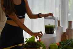 年轻的女人搅拌机使健康的绿色奶昔厨房健康的吃概念