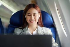 肖像成功的亚洲女商人女企业家正式的西装飞机坐在业务类座位电脑移动PC飞行