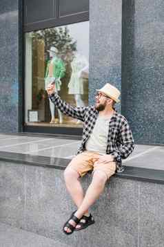 有胡子的男人。需要自拍智能手机漫步市中心提出了现代城市建筑享受休闲时间人城市生活方式技术概念