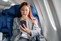 肖像成功的亚洲女商人女企业家正式的西装飞机坐在业务类座位吃智能手机飞行