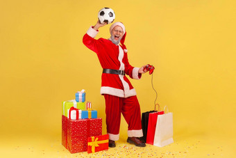 完整的长度男人。灰色的胡子圣诞老人老人服装提高了手臂足球球持有操纵杆庆祝赢得足球视频游戏